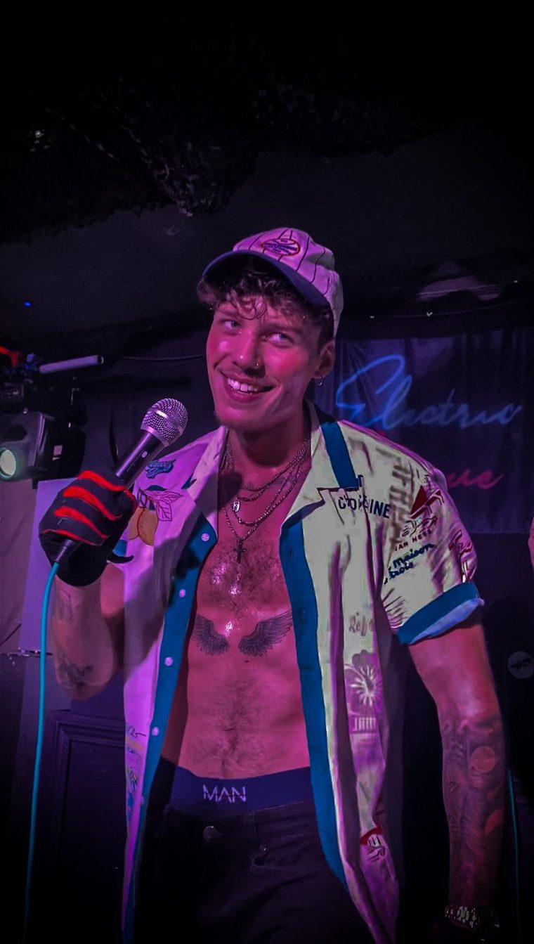 Flexx Carter grinning on stage at Electric Avenue, mic in a gloved hand